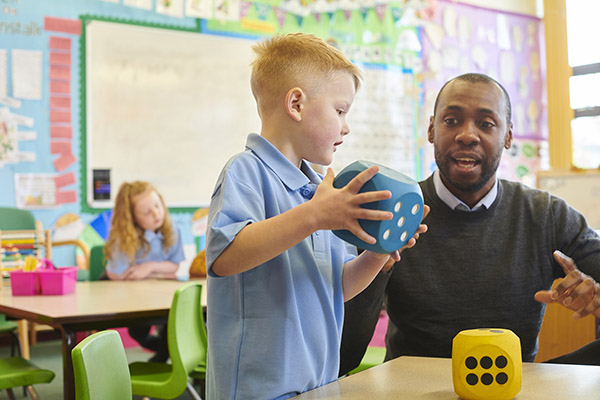 A teacher helps a young child who is holding a large dice in math class