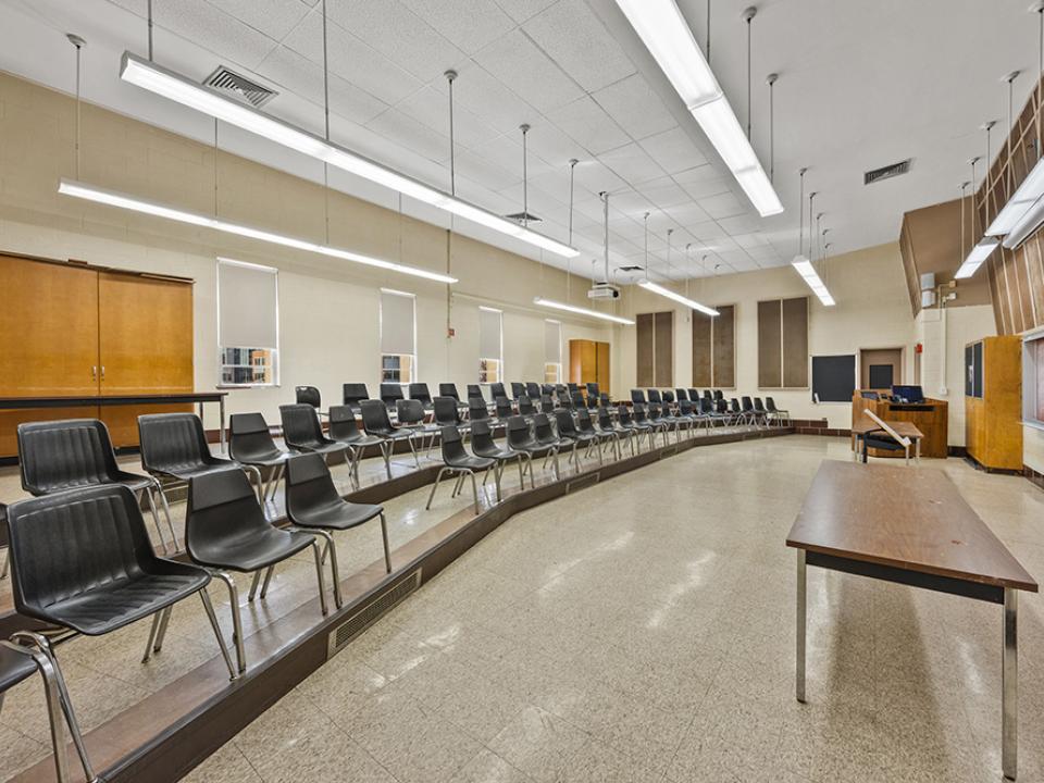 Classroom with two tiers of seats in rows in front of lectern and board on wall