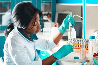 Biology Student in lab coat and protective wear testing of patient samples in modern test laboratory.