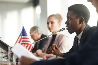 A male in a suit speaks into a microphone at a political meeting