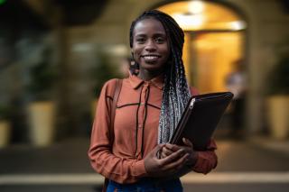 An African-American female student smiles outside of a building
