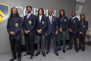 Coppin State University President Anthony L. Jenkins stands with six male students wearing dark Presidential Scholar blazers and cardigans, posing for a formal photo in front of a wall with the Coppin logo.